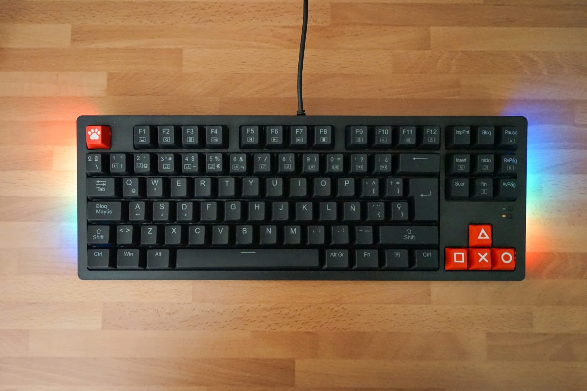 A gaming keyboard with glowing RGB lights on a wooden desk